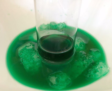 Green liquid on a plate being sucked into an upside down cup due to thermal expansion