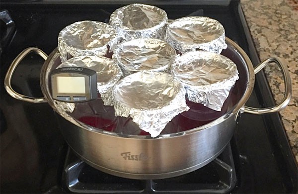Seven cups of Red 40 solution are covered with aluminum foil and placed in a pot of boiling water