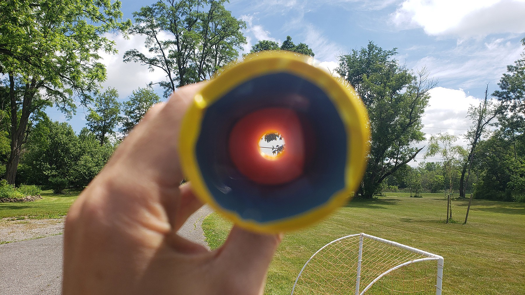 Scenery with trees, clouds, and a power line. Part of the picture shows the view through the telescope, where the leaves and power line are magnified. 