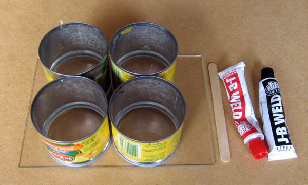 Four tin cans, a small glass pane, a popsicle stick, and two tubes of a two-part epoxy