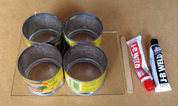Four tin cans, a small glass pane, a popsicle stick, and two tubes of a two-part epoxy