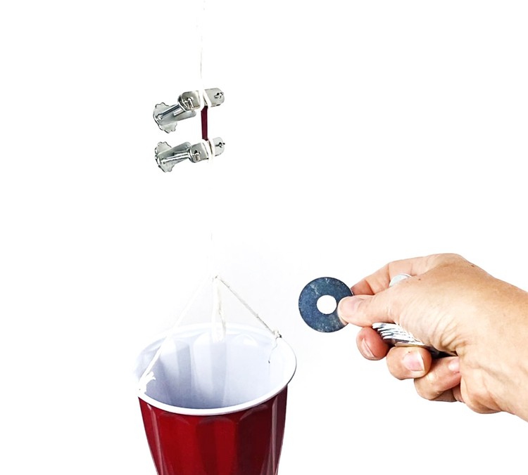 One compressor clamp containing the sample strip is attached to a hook. To the second compressor clamp containing the sample a little bucket is attached with a string. A hand is holding a metal washer next to the little bucket. 