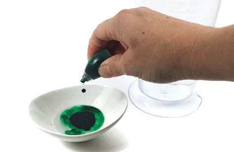 Hand squeezing food color from a bottle into a small bowl filled with water.