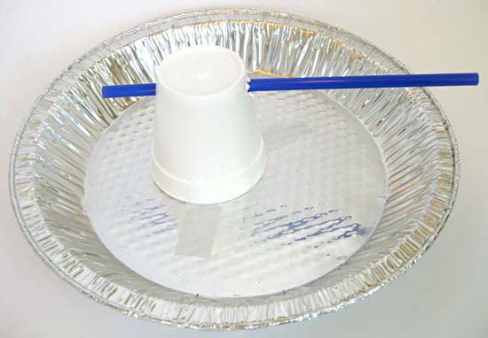 A styrofoam cup that is skewered by a straw near the base is taped upside-down to an aluminum foil pie pan