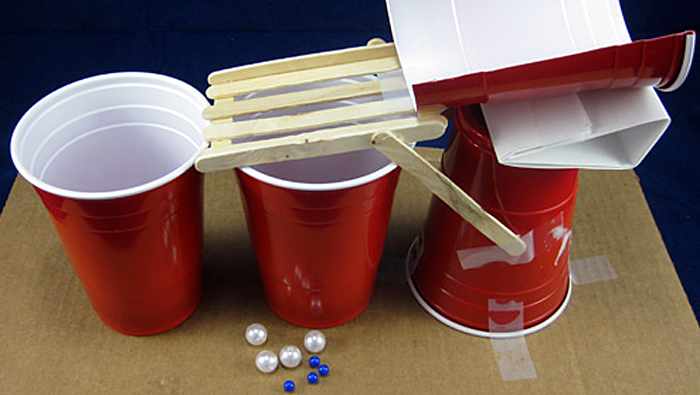 A marble sorting machine made from popsicle sticks, plastic cups and tape