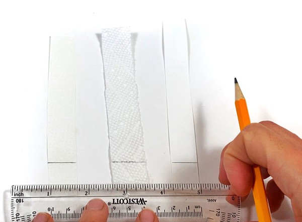 Three strips of paper are lying on a table. Each paper strip has a drawn pencil ine about 1 cm from the bottom.