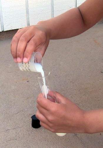 Milk being transferred from a medicine cup to a test tube