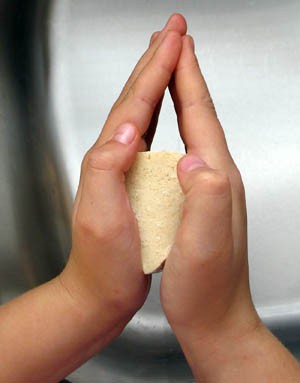 A tofu cube is squeezed between the palms of two hands