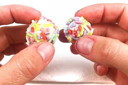 Two hands holding two different aluminum balls that are covered in sprinkles.