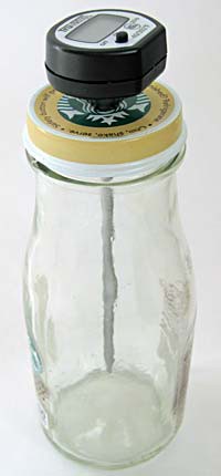 A probe thermometer is inserted into the lid of a glass bottle