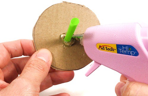 Person putting hot glue around a straw that is inserted through a hole in a cardboard circle.