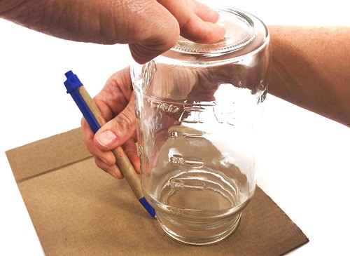 Person tracing the opening of a jar on a piece of cardboard.