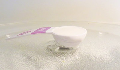 A tablespoon filled with a white liquid mixture sits on a glass plate in a microwave