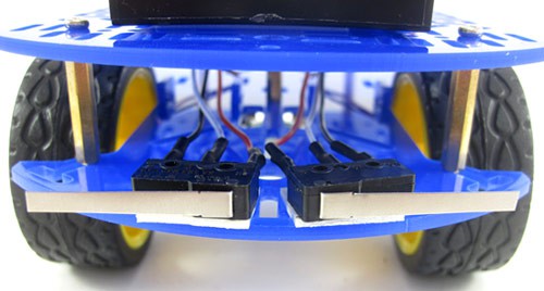 Two lever switches are attached to the bottom front chassis of an object avoiding robot using double sided tape