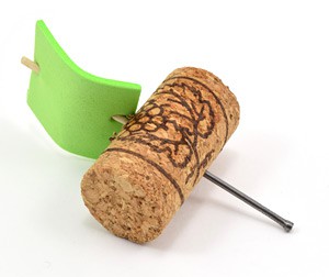 A cork cylinder has a nail inserted into its side with a toothpick and green foam inserted into the opposite side