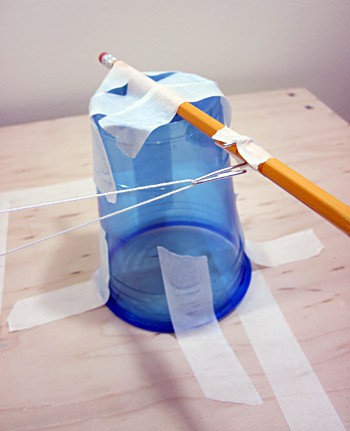 Photo of an upside down cup taped to a tabletop and a pencil taped to the bottom of the cup