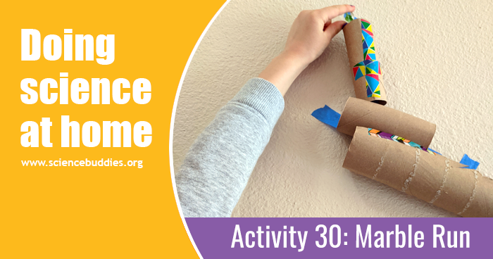 Student putting a marble into the top of a homemade marble run made from cardboard tubes