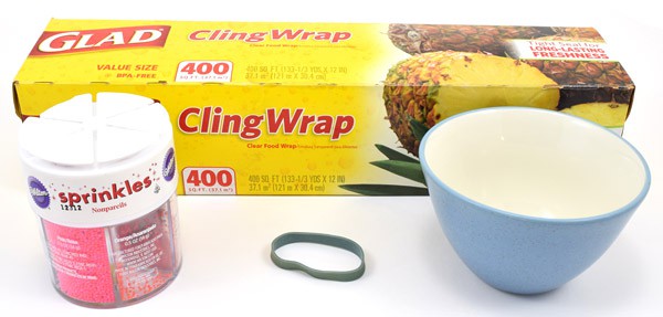 Plastic wrap, a can of sprinkles, a rubber band, and a small bowl