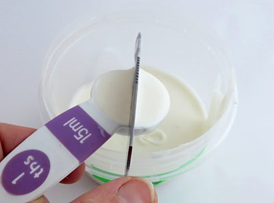 A tablespoon filled with a white liquid mixture is leveled with a metal knife