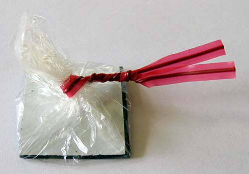A twist tie secures plastic wrap surrounding a square of magnetic tape