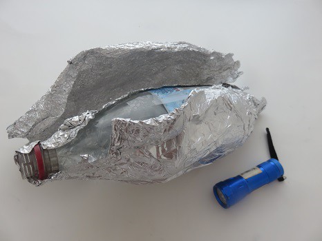 A plastic bottle wrapped in foil with a little flashlight next to it