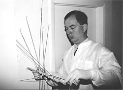 Photo in black and white of a forensic scientist examining blood spatter in a room