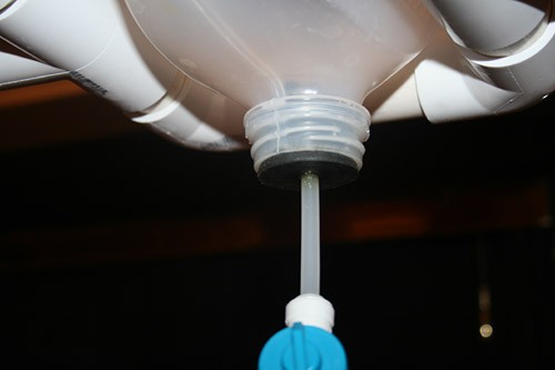 A plastic tube is inserted into the center of a rubber stopper is plugged into the mouth of a plastic jug