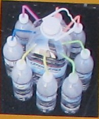 A failed desalination device where eight water bottles evaporate water through straws into a larger bottle in the center