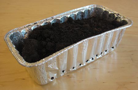 Drainage holes are created at the base of an aluminum bread pan that has been filled with soil