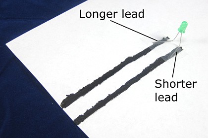 Leads of an LED are taped to conductive ink lines on a piece of paper