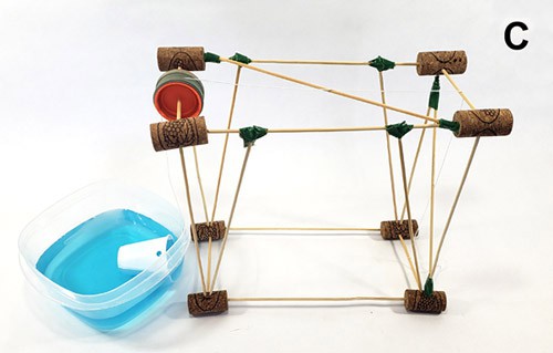 A cup attached to a pulley suspended from a frame of wooden skewers and cork